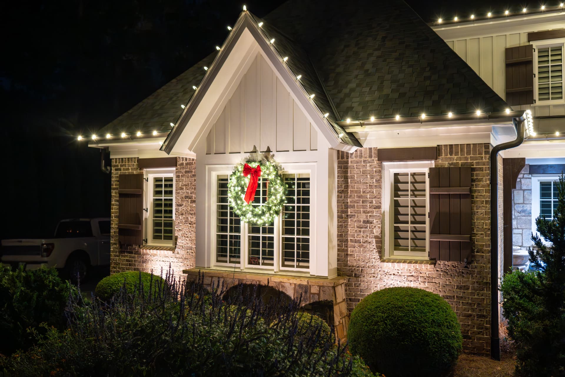 Two-story brick home glowing with professionally installed Christmas lights at night